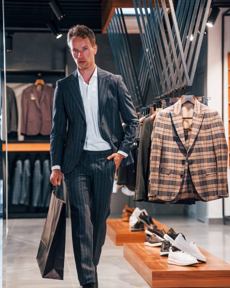 Shopping day. Young guy in modern store with new clothes. Elegant expensive wear for men.