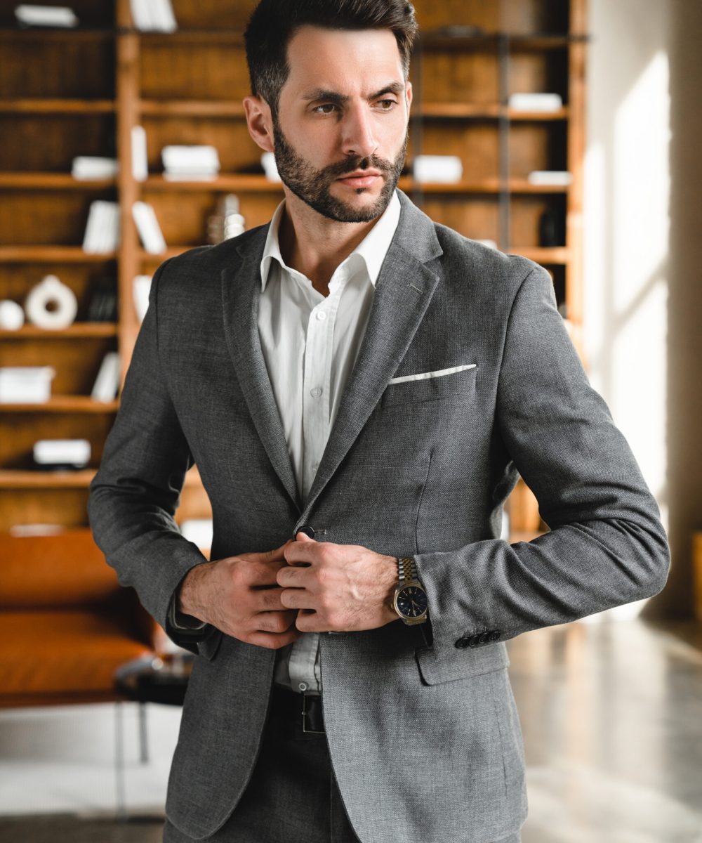 Vertical shot of successful young businessman in grey formal suit posing in modern expensive office